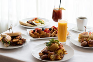 Five plates of breakfast dishes and three beverages on a white table in Concord, MA restaurant