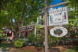 Concord Colonial Inn sign in Concord, MA infront of the Inn with large blossomed trees and patriotic outdoor decoration