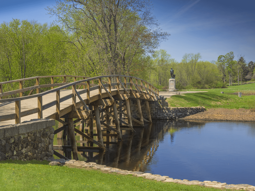 Old North Bridge in Concord, MA a wooden bridge over water with a view of a field and trees