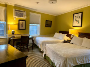 Guest room with two double beds with white comforter and green bed skirt, bright green walls and desk area in the historic Concord, MA hotel