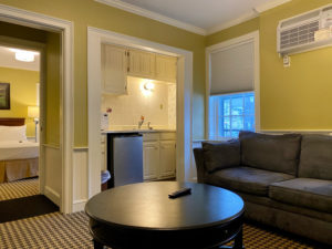 Suite at historic Concord, MA hotel with a grey couch black coffee table, kitchenette area and a view of the bedroom