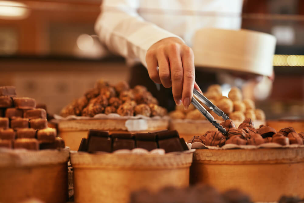 Concord confectionery shop employee uses tongs to gather some chocolates for a customer.